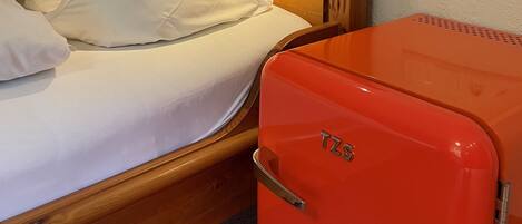 A bed with white bedding, a wooden headboard, a wall-mounted lamp, and a red suitcase.