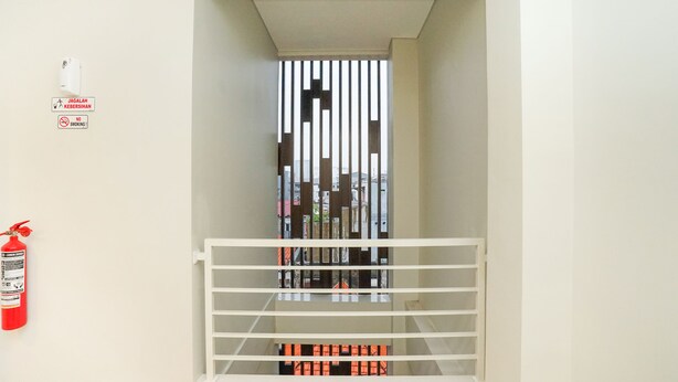 A narrow corridor with a white railing, a fire extinguisher, and a smoke detector on the wall. - Super OYO Capital O 614 Graha 8 Syariah (Surabaya)