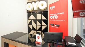 A reception desk with a computer, a sign for OYO Hotels, and a promotional poster for OYO app benefits. - Super OYO Capital O 614 Graha 8 Syariah (Surabaya)