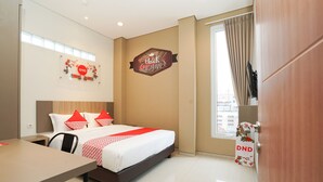A hotel room with a bed, a desk, a TV, and a window with curtains. - Super OYO Capital O 614 Graha 8 Syariah (Surabaya)
