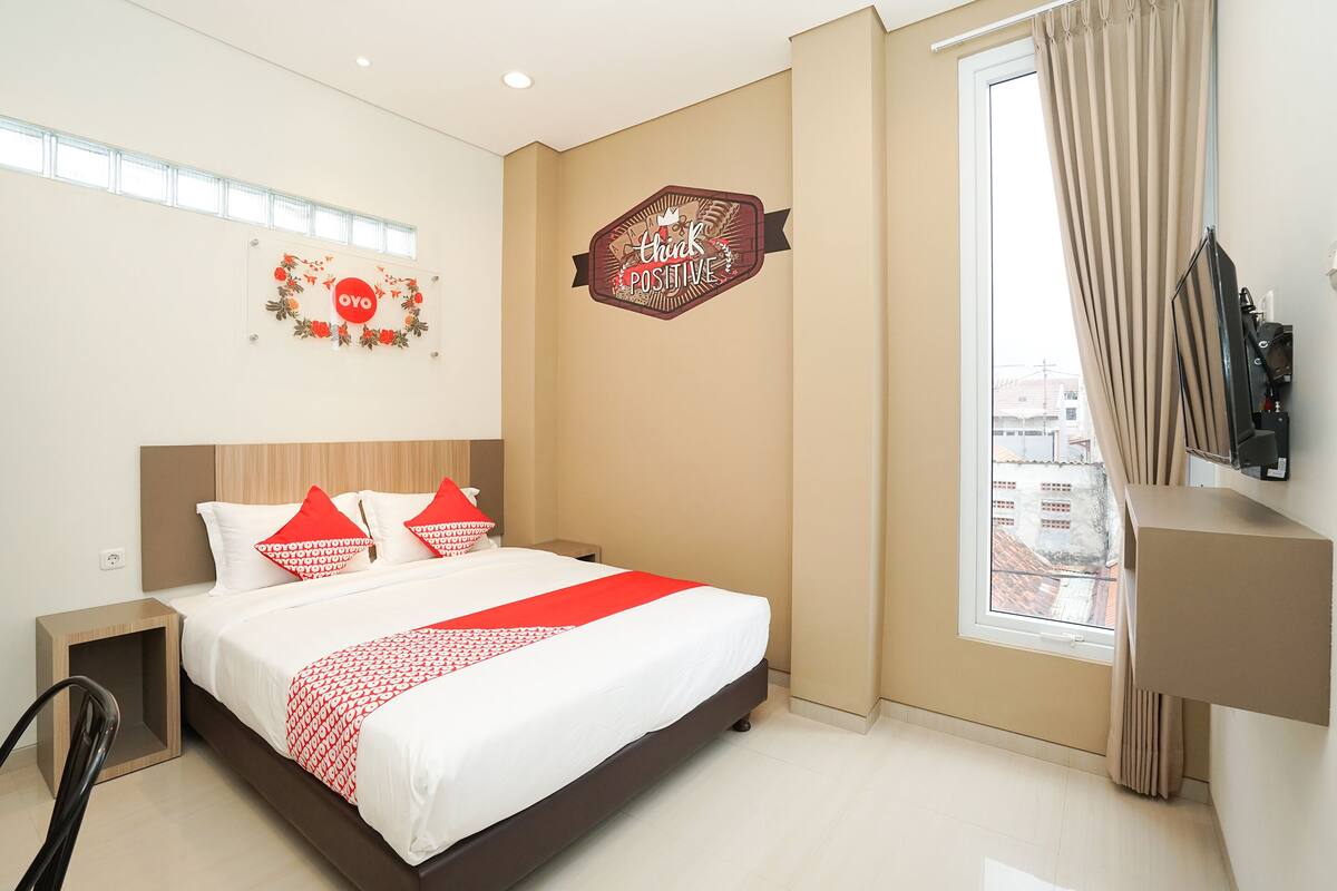 A hotel room with a bed, a nightstand, a TV, and a window with curtains.