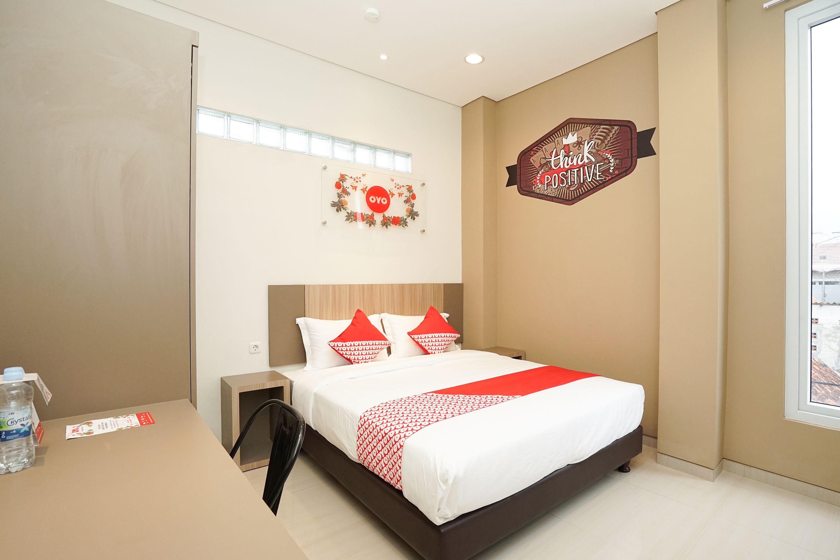 A hotel room with a bed, a nightstand, a water bottle, and a sign on the wall.