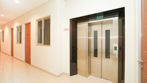 A hallway with doors, a glass elevator, and a sign above the elevator. - Super OYO Capital O 614 Graha 8 Syariah (Surabaya)