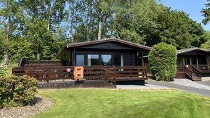 Eine Holzhütte mit einer Holzterrasse, einer kleinen Veranda und einem großen Fenster.