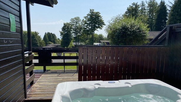 Ein Whirlpool auf einer Holzterrasse mit Blick auf einen eingezäunten Garten und Bäume.