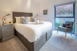 Un dormitorio moderno con una cama grande, mesitas de noche, una silla y vistas al exterior.