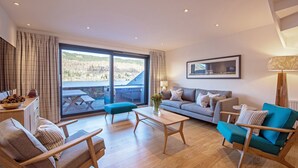 Een moderne woonkamer met een bank, fauteuils, een salontafel en uitzicht op een balkon met een houten terras.