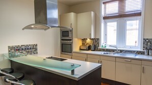Une cuisine moderne dotée d’un îlot central en verre, d’appareils électroménagers en acier inoxydable et d’une fenêtre avec des stores.