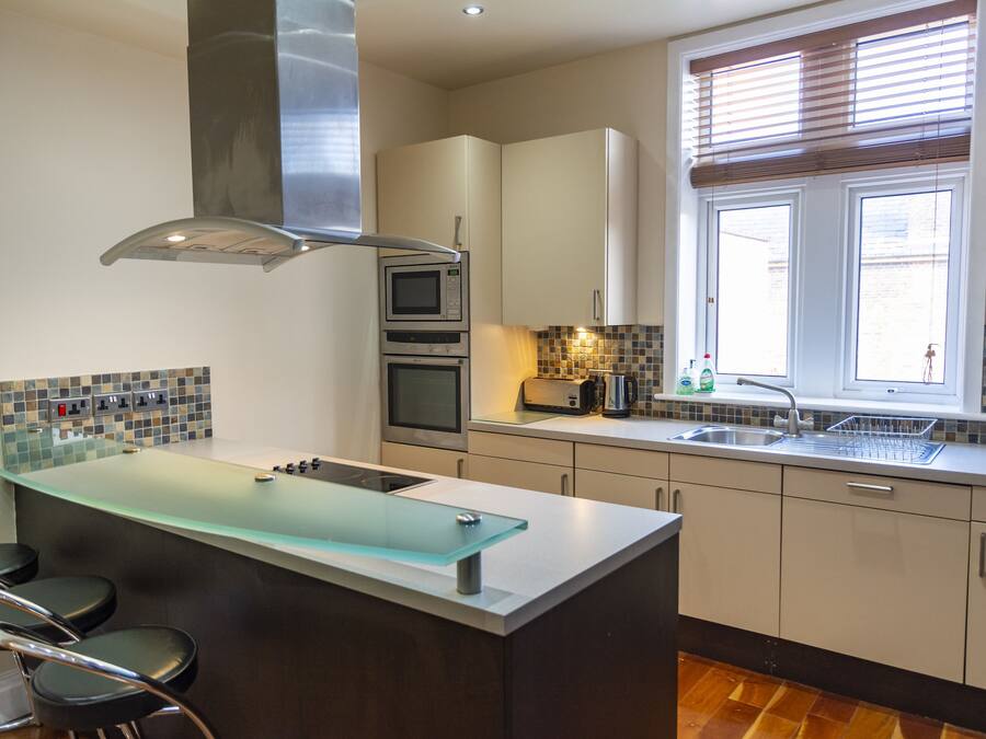 A modern kitchen with a glass island, stainless steel appliances, and a window with blinds.