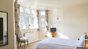 Une chambre avec un grand lit, une chaise, un téléviseur et une fenêtre avec des rideaux.