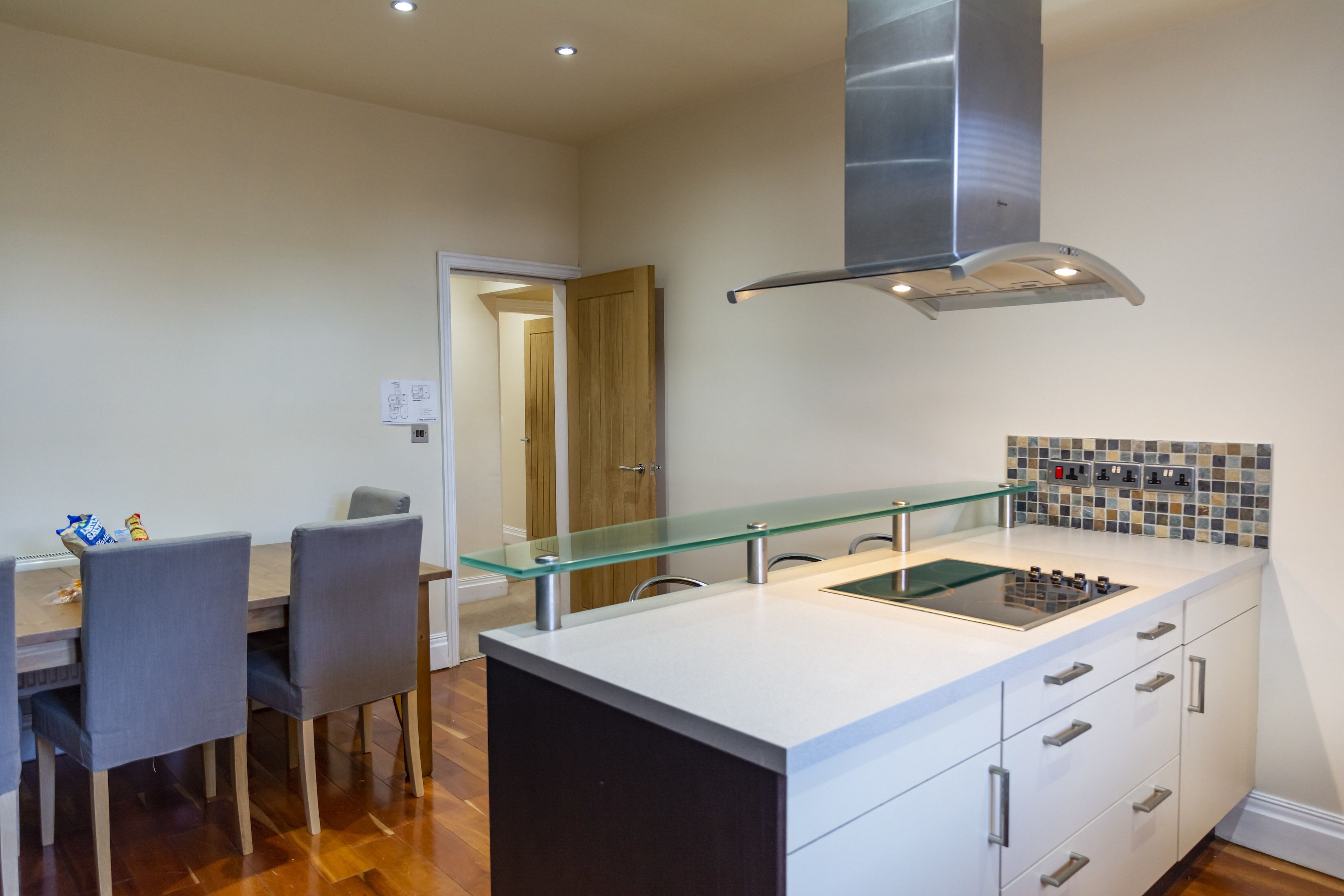 A modern kitchen with a glass-top island, stainless steel range hood, and a tiled backsplash.