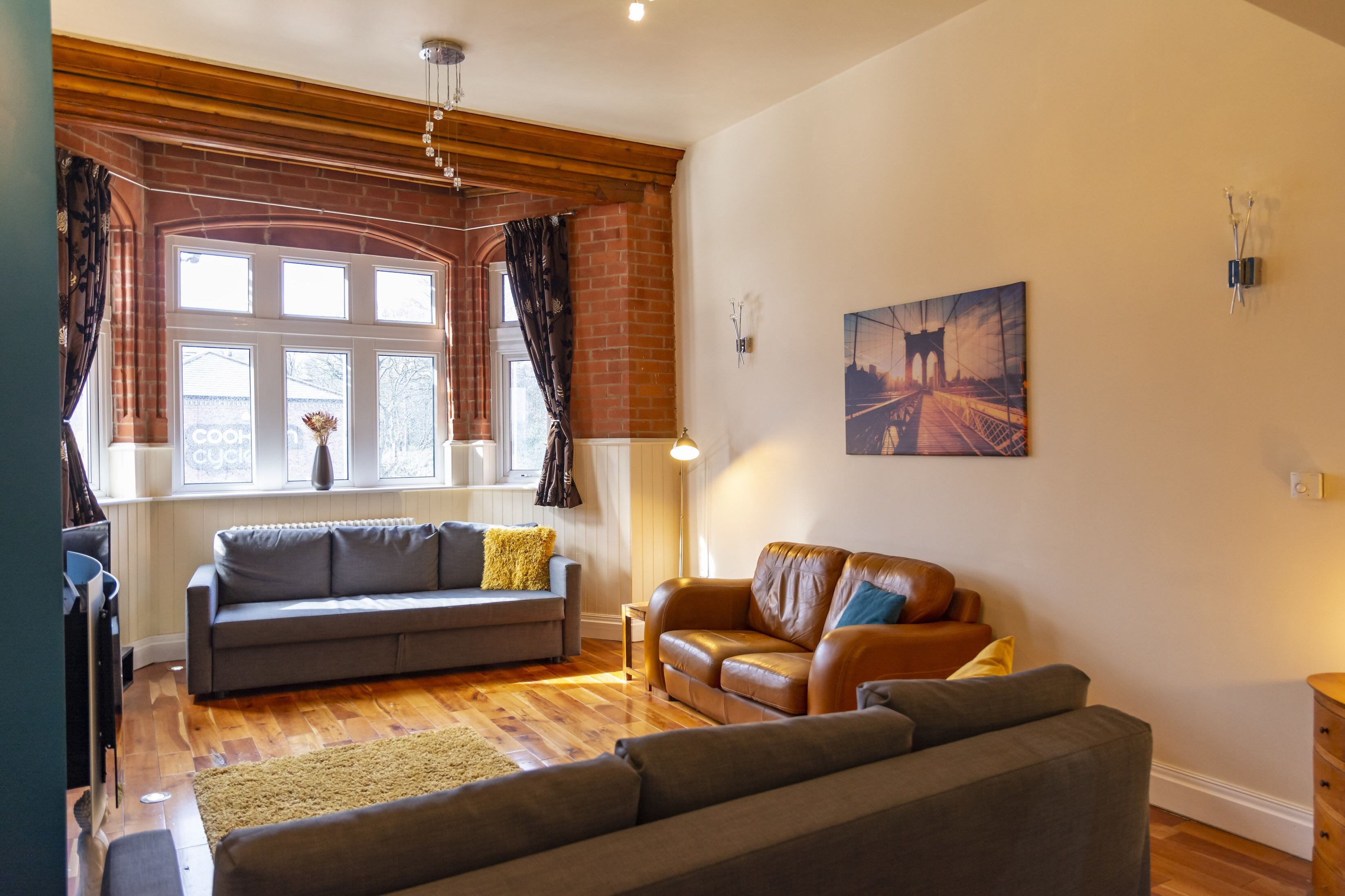A living room with a grey sofa, a brown leather sofa, and a wooden floor.