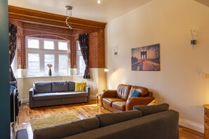 A living room with a grey sofa, a brown leather sofa, and a wooden floor. - Whitefield Charm Cozy 2 Bedroom Apartment Sleeps 8 (Manchester)
