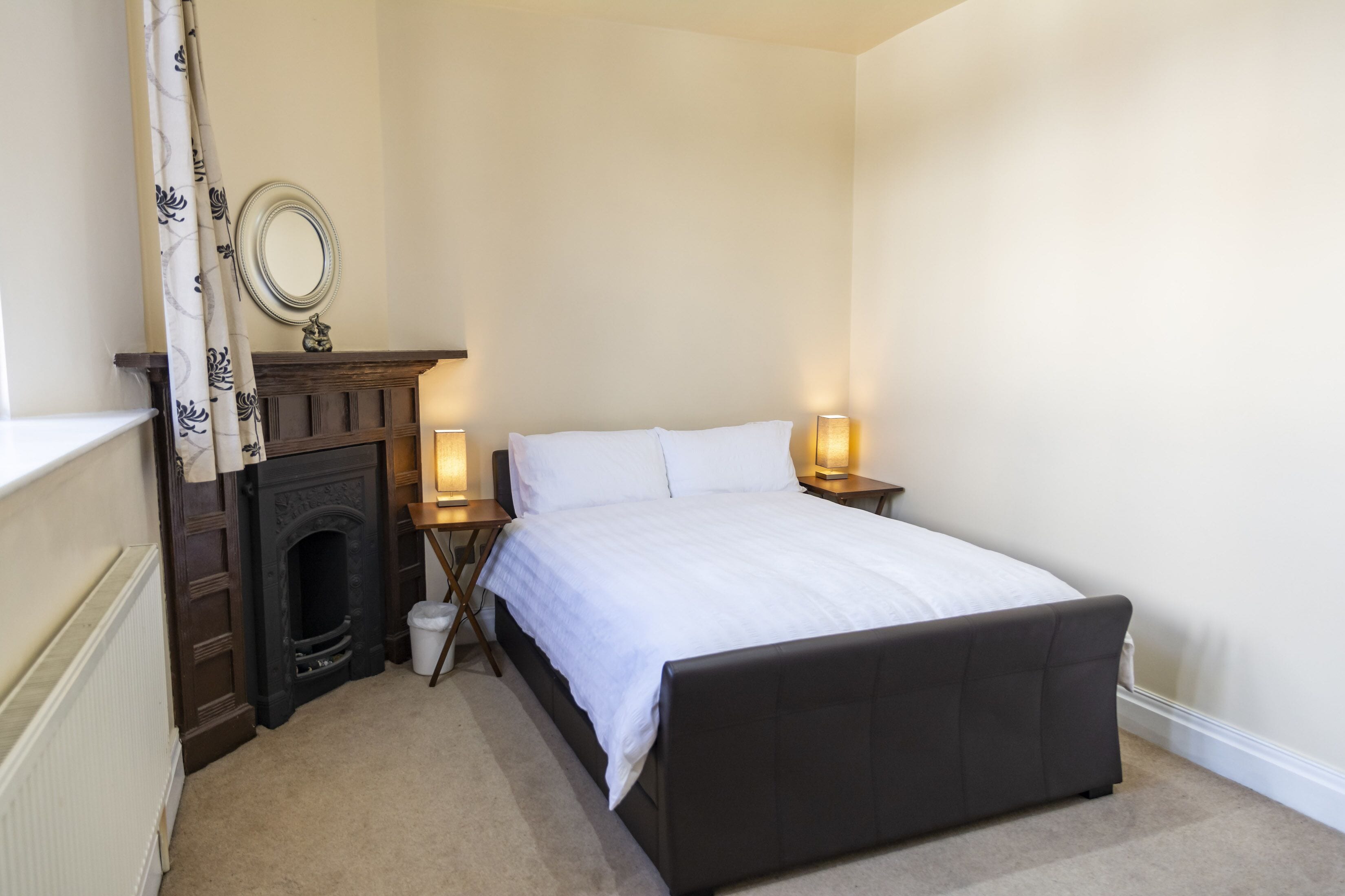 Een slaapkamer met een bed, een openhaard, een spiegel en twee bedlampen.