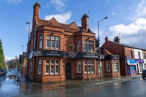 A red-brick building with multiple windows and a black awning displaying 'IQS' and 'Chartered Quantity Surveyors'. - Whitefield Charm Cozy 2 Bedroom Apartment Sleeps 8 (Manchester)