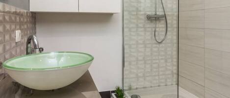A modern bathroom with a glass-enclosed shower, a green glass sink, and a small potted plant on the counter.