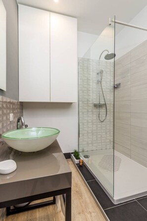 A modern bathroom with a glass-enclosed shower, a green glass sink, and a small potted plant on the counter. - Apartments Kappa (Rijeka)