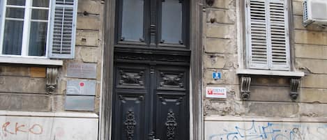A building with a black ornate door, multiple windows with shutters, and a visible sign indicating a dentist.