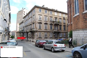 A street with parked cars and a building with a main entrance marked by a red arrow. - Apartments Kappa (Rijeka)
