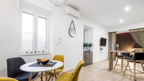 A modern living room with a dining area, featuring a round table, yellow chairs, a clock, and a TV. - Apartments Kappa (Rijeka)