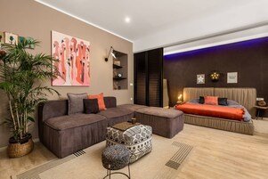 Una sala de estar moderna con un sofá seccional, un otomán estampado, una planta grande en maceta y una obra de arte colgada en la pared.