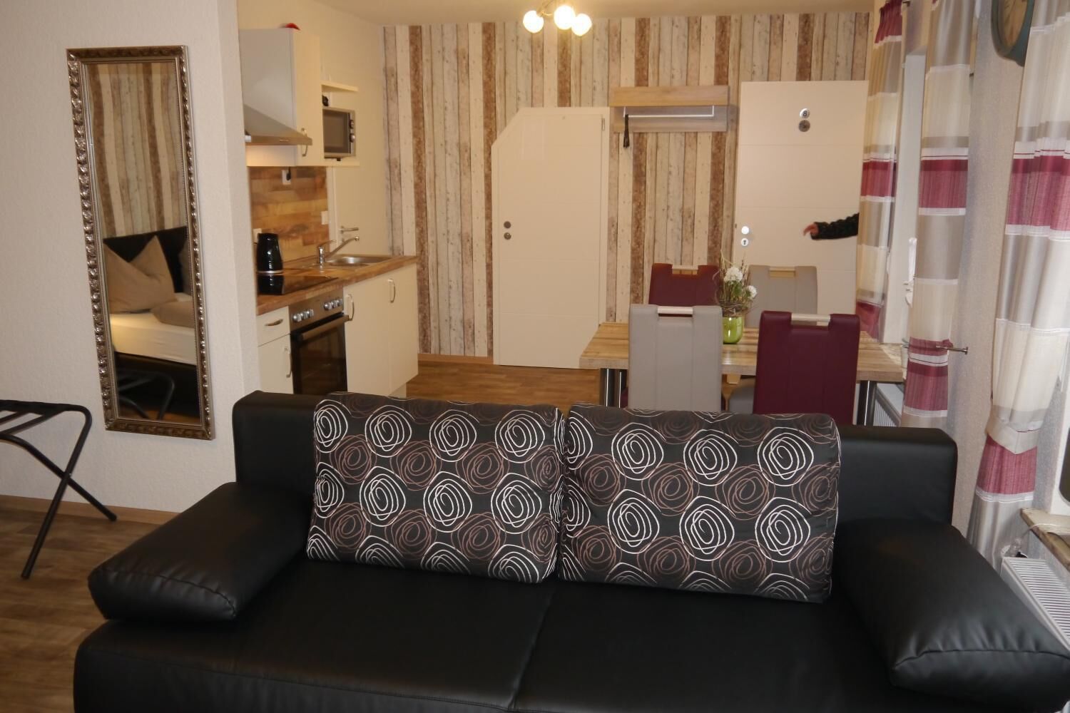 Una sala de estar con un sofá de cuero negro, una mesa de comedor de madera y una zona de cocina con microondas y estufa.