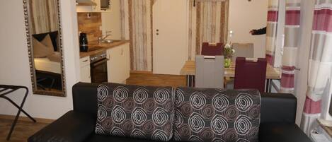 A living room with a black leather sofa, a wooden dining table, and a kitchen area with a microwave and stove.