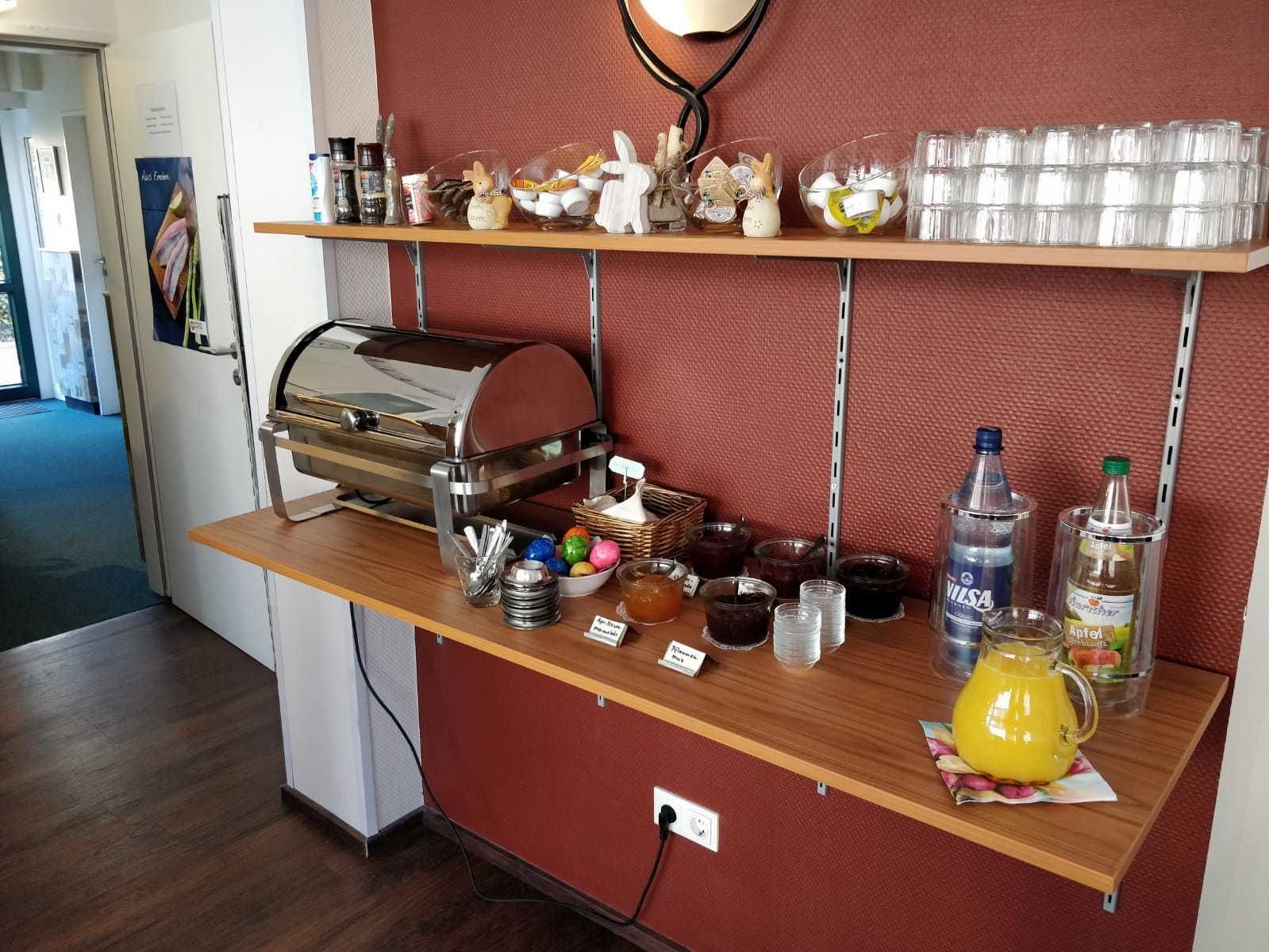 Una barra de buffet con una máquina de café, diferentes recipientes de comida y bebidas sobre una encimera de madera.