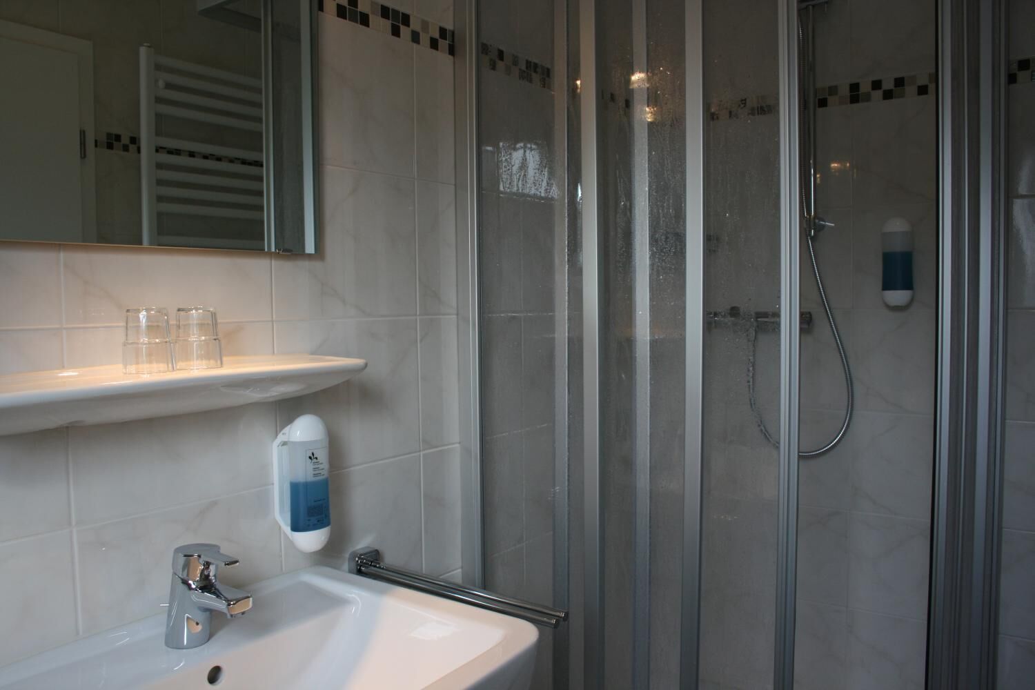 Un baño moderno con cabina de ducha de vidrio, un lavabo blanco y un estante con vasos.