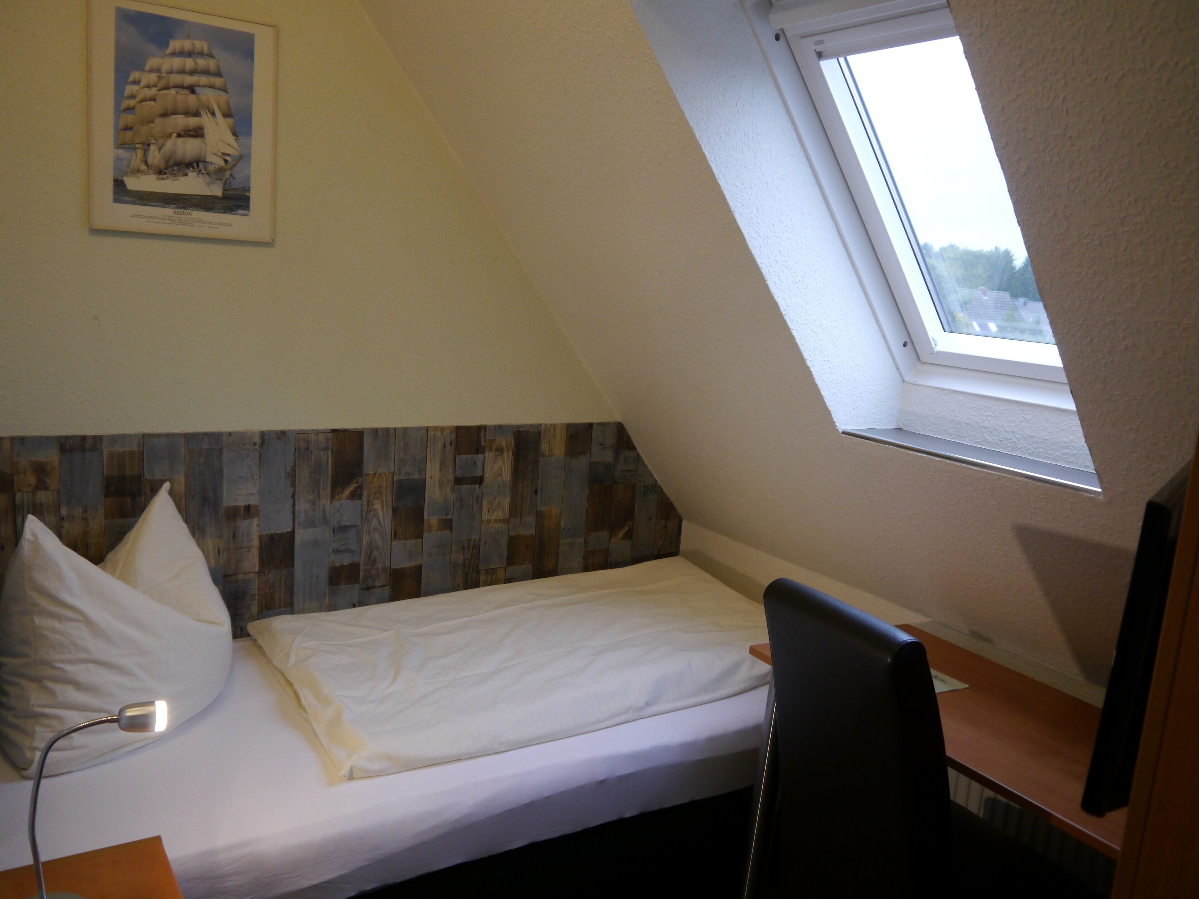 Ein kleines Zimmer mit einem Einzelbett, geneigter Decke und einem Oberlicht.