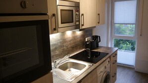 Una cocina compacta con microondas integrado, cafetera y lavadora.