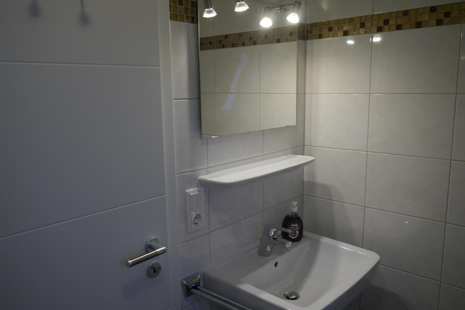 A modern bathroom with a white sink, a mirror above it, and a shelf.