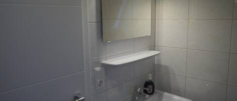 A modern bathroom with a white sink, a mirror above it, and a shelf.