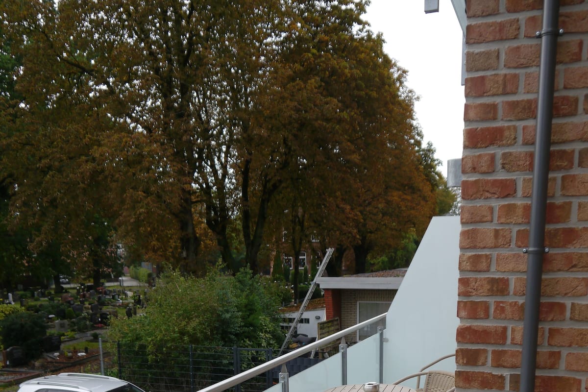 A balcony with wicker chairs and a table, overlooking a street with a parked car and trees.