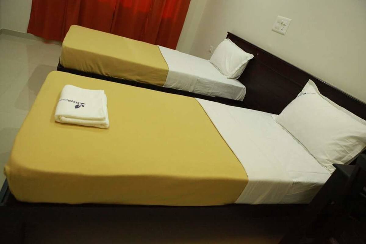 Dos camas individuales con ropa de cama amarilla y blanca, una toalla doblada en la cama de la izquierda y una almohada blanca en la de la derecha.