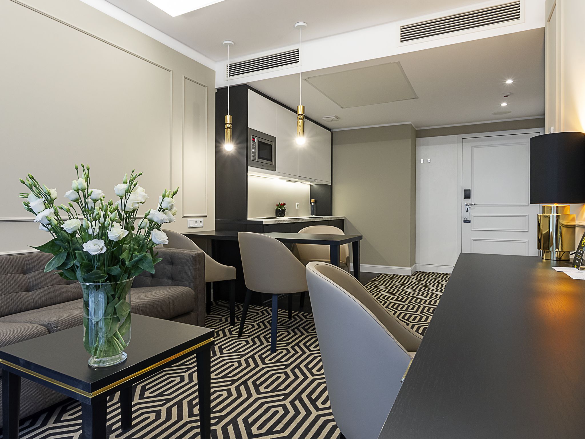 A modern hotel room with a dining area, a sofa, a coffee table, and a vase of flowers.