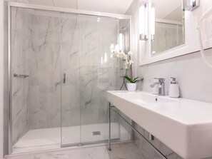 A modern bathroom with a glass-enclosed shower, a white sink with a mirror, and a potted orchid. - Vacation Club - Baltic Park Fort (Swinoujscie)