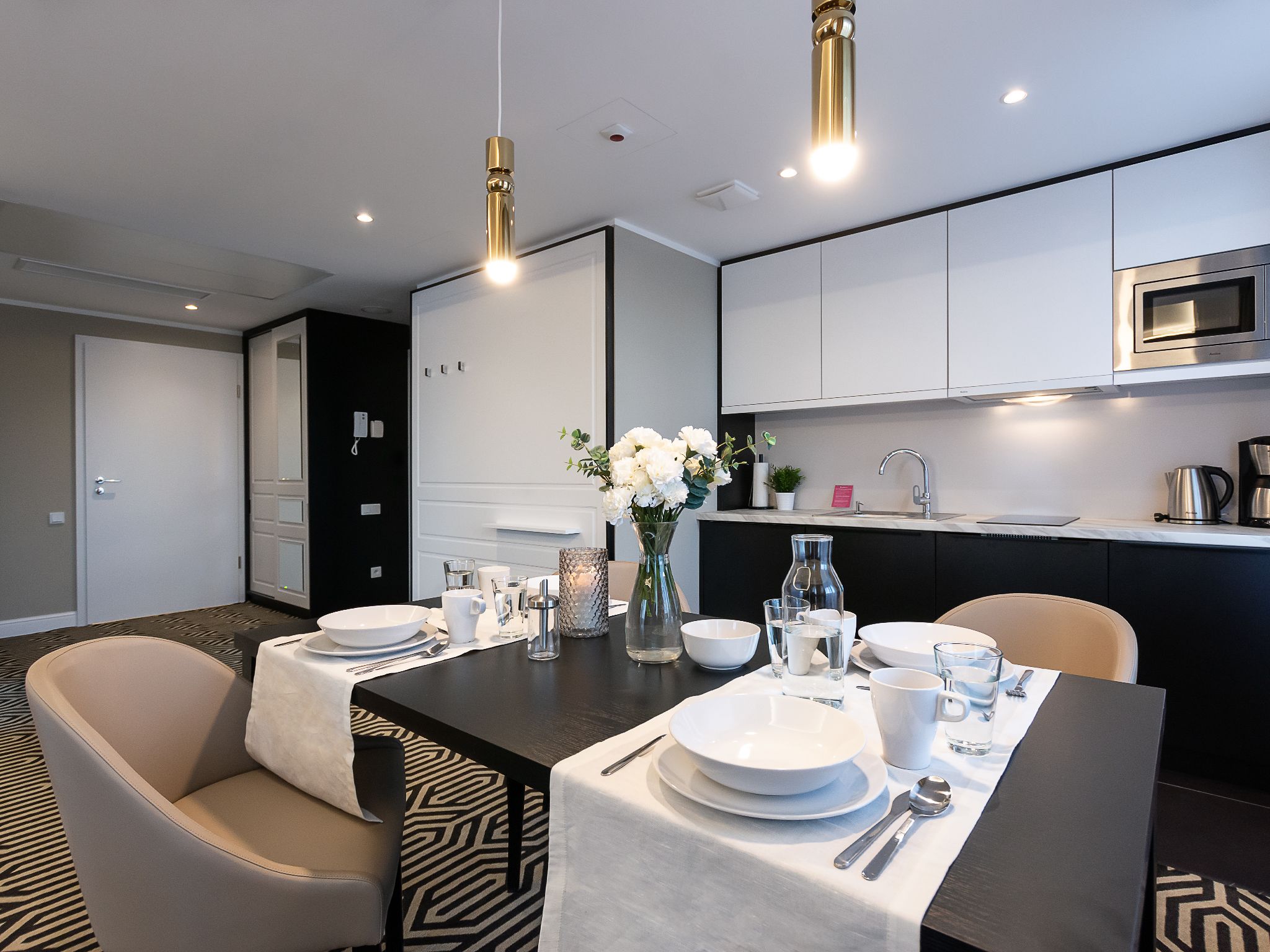 A modern dining area with a table set for four, a kitchen with stainless steel appliances, and a patterned carpet.