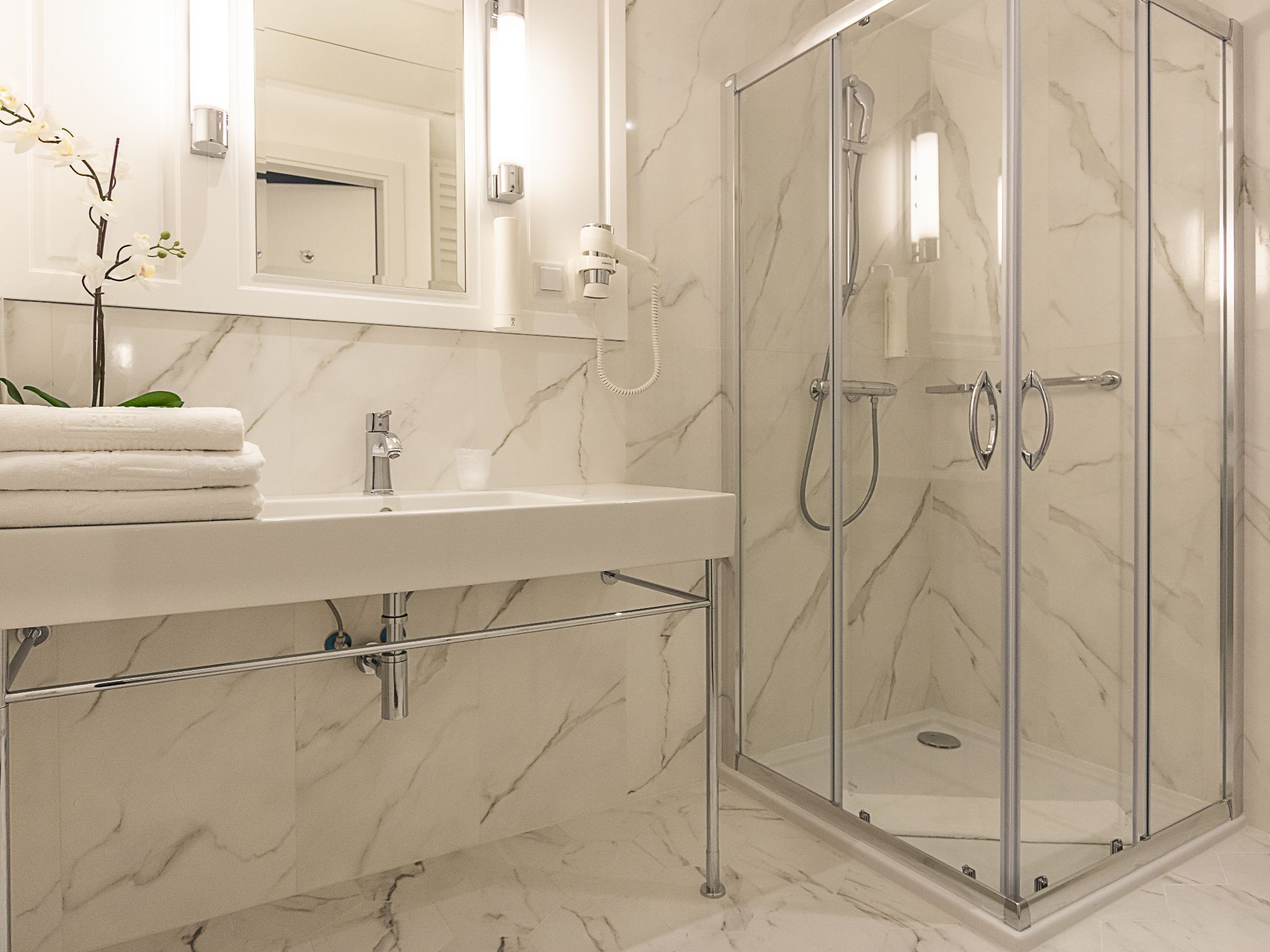 Een moderne badkamer met een marmeren wastafel, een douche met glazen wanden en een spiegel boven de wastafel.