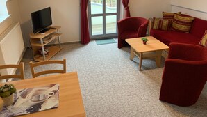 A cozy living room with a red sofa, a wooden coffee table, a TV on a stand, and a dining table with chairs. - Toplicht - Villa Doris (Koserow)