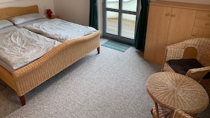 A bedroom with a large bed, a wicker chair, a wooden cabinet, and a view through a glass door. - Toplicht - Villa Doris (Koserow)