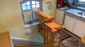 A kitchen with a wooden chair, a window with blinds, a coffee maker, and a patterned rug. - Toplicht - Villa Doris (Koserow)
