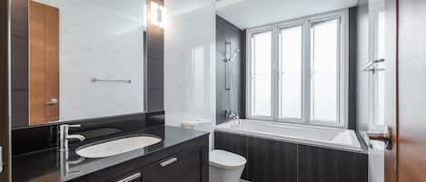 A modern bathroom with a dark wood vanity, a white sink, a toilet, and a bathtub.