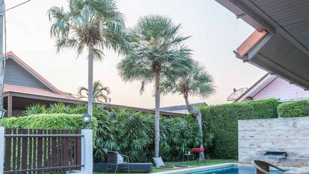 Un jardin avec une piscine, des palmiers et un mur en pierre.