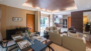 Un salon moderne comprenant un coin repas, un ensemble de canapés et une cuisine visible à travers une porte ouverte.