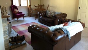A living room with a brown leather sofa, a red armchair, and a dining table with chairs. - Thatched Cottage, West Dorset (Dorchester)
