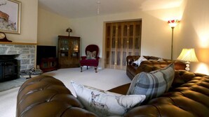 A living room with a fireplace, a red armchair, a brown leather sofa, and a wooden cabinet. - Thatched Cottage, West Dorset (Dorchester)
