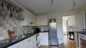 A kitchen with white cabinets, a stainless steel refrigerator, a microwave, and a sink with a wooden soap dish. - Thatched Cottage, West Dorset (Dorchester)