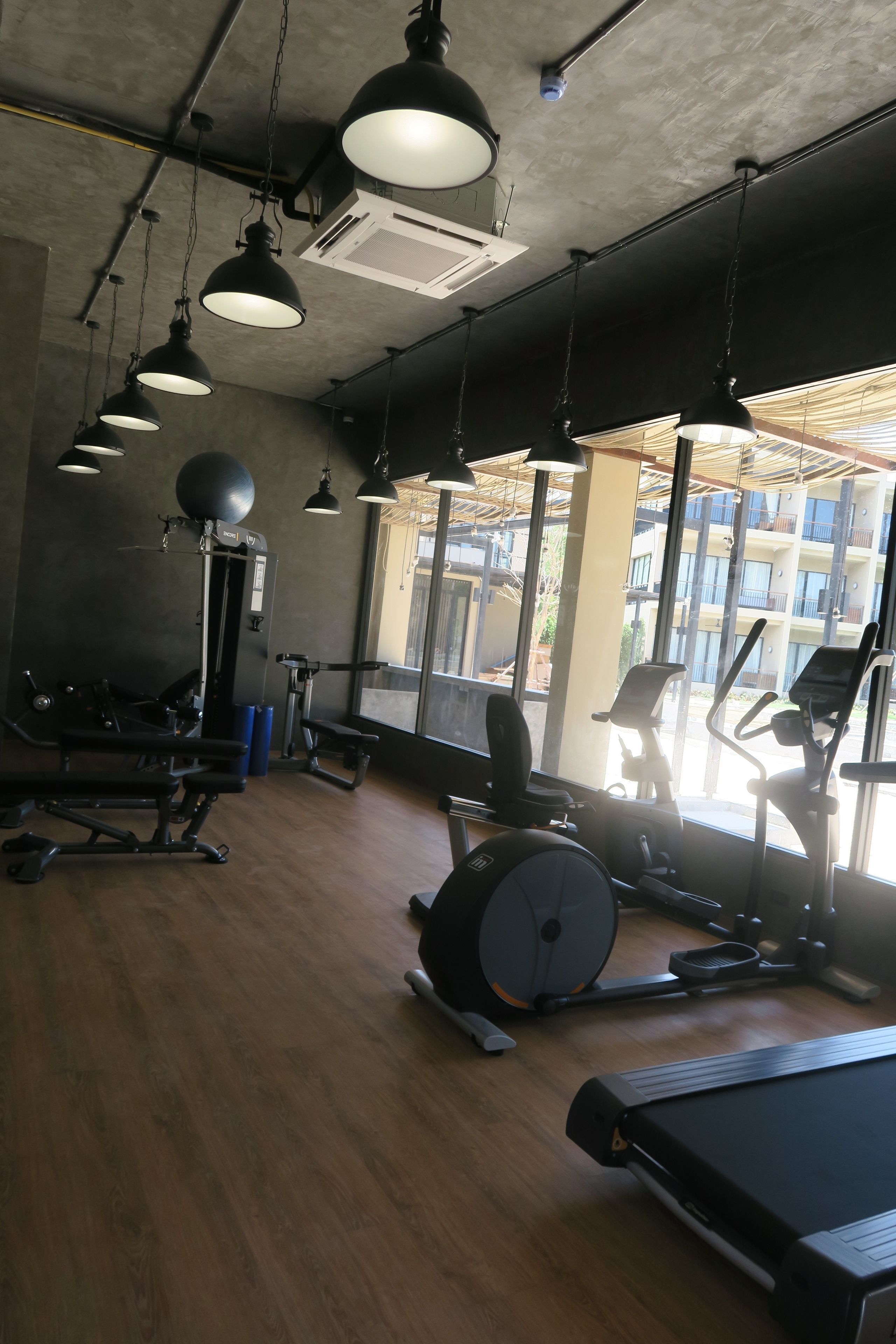 A gym with exercise equipment, large windows, and hanging lights.