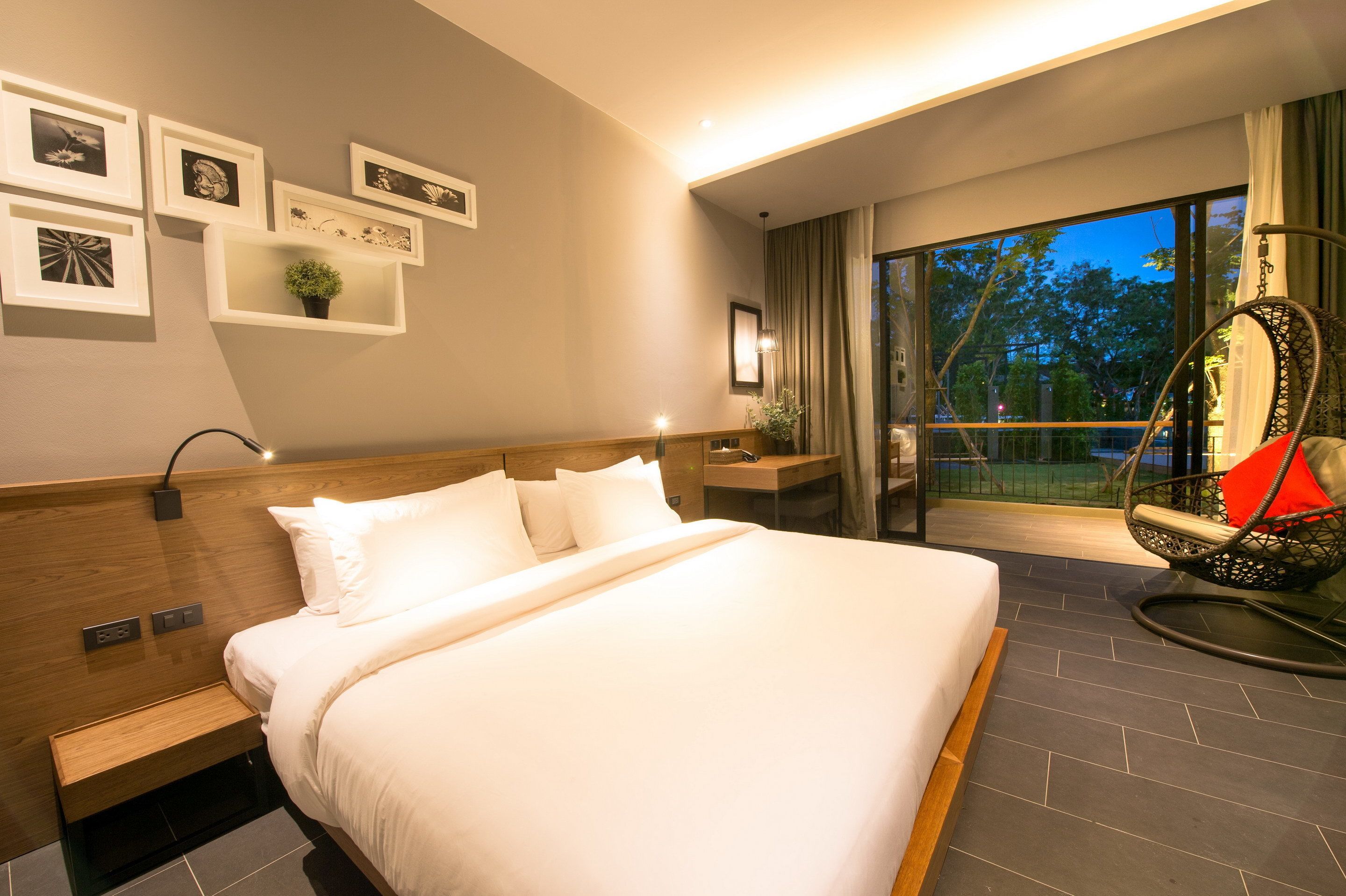 Una habitación de hotel moderna con una cama grande, un sillón colgante y un balcón con vistas a árboles.